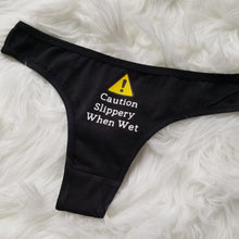 Load image into Gallery viewer, Caution Slippery When Wet text with caution sign above on a black thong
