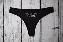 Load image into Gallery viewer, Women's black thong with the text property of Shane with a red heart next to the name. Text is white.