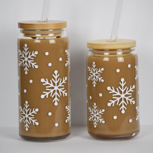 Two glass cans with bamboo lids and glass straws. Decorating the cans are white snowflakes and small white dots of snow.