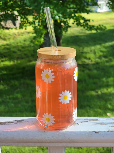 Glass can with bamboo lid and glass straw with white and yellow daisies.
