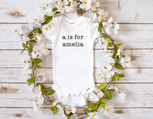 Load image into Gallery viewer, White baby bodysuit with text &quot;a is for amelia&quot; in black text. Customizable with child&#39;s name.
