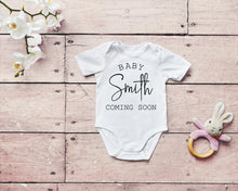 Load image into Gallery viewer, White baby bodysuit with text &quot;baby smith coming soon&quot;. The name smith is in a cursive font.
