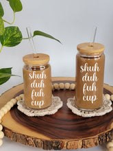 Load image into Gallery viewer, Two can shaped glass cups with bamboo lids and glass straight straws sit on coasters on a wooden lazy Susan. Cans are shown in 16oz and 20oz sizes. Both cans have the text shuh duh fuh cup on the front in white cursive font.
